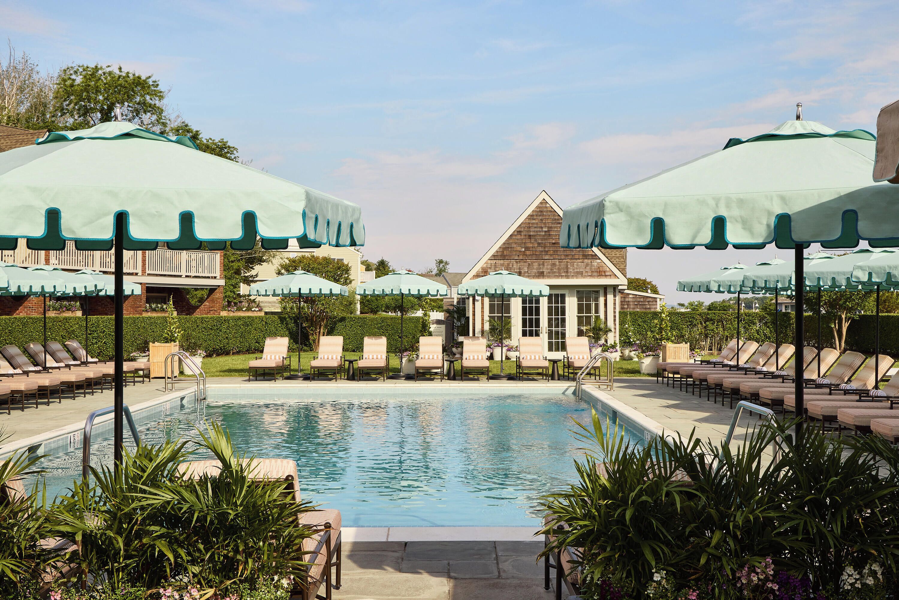 A pool area with lounge chairs and umbrellas, a small building, and a clear sky.