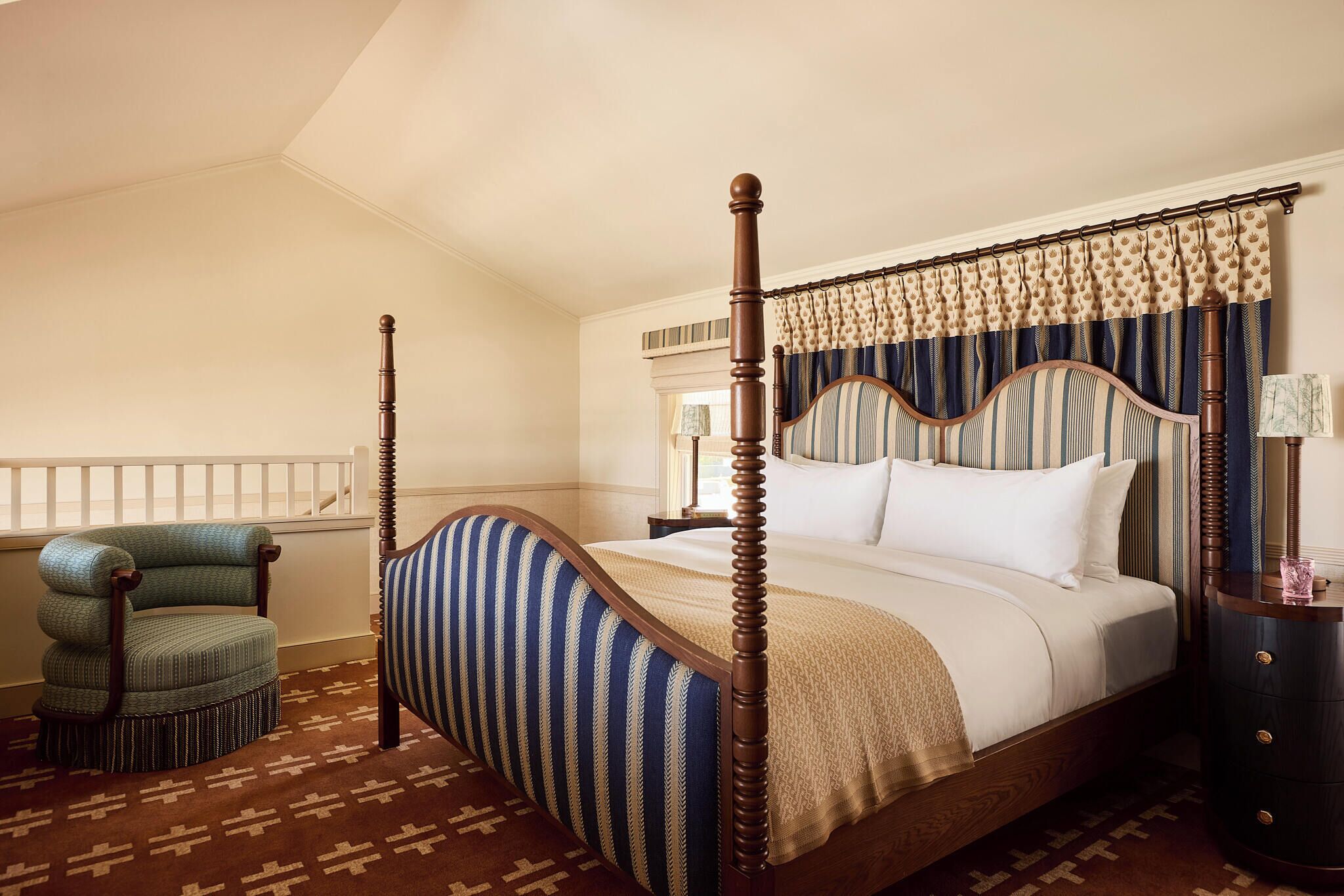 A four-poster bed with a wooden frame, a striped upholstered chair, and a patterned carpet.