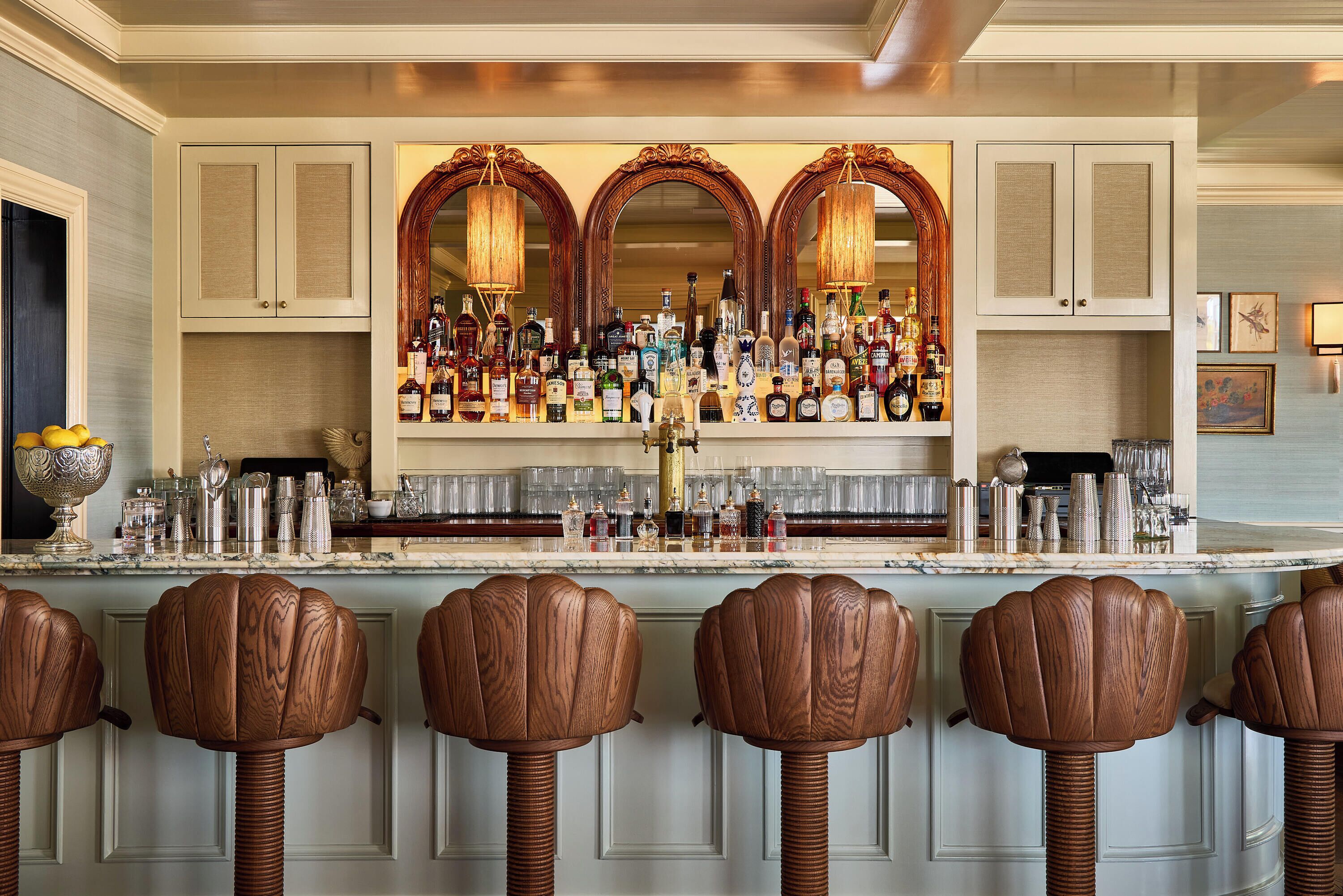A bar area with a marble countertop, multiple liquor bottles, and wooden bar stools.
