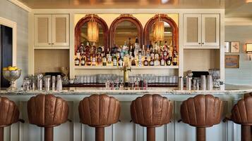 A bar area with a marble countertop, multiple liquor bottles, and wooden bar stools.