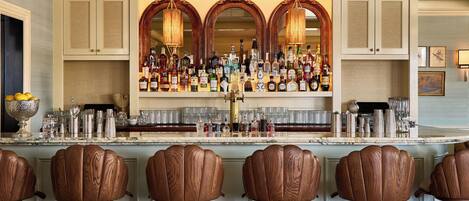 A bar area with a marble countertop, multiple liquor bottles, and wooden bar stools.
