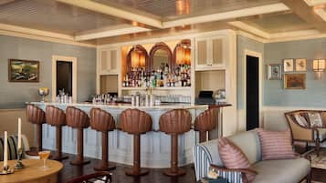 Un área de bar con taburetes, una barra y una zona de estar con sofá y sillas.
