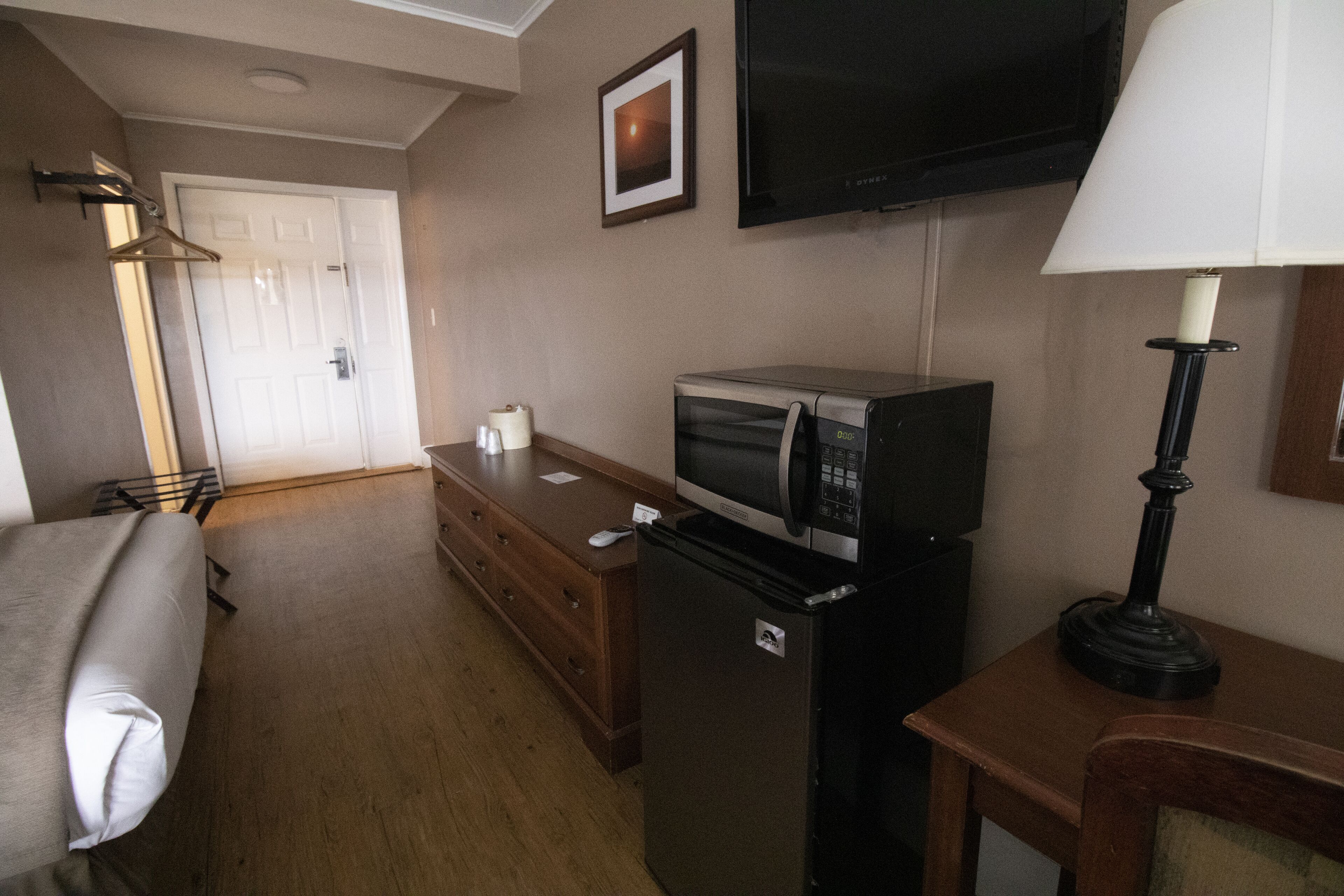 A hotel room with a bed, a dresser, a microwave, a refrigerator, a television, and a lamp.