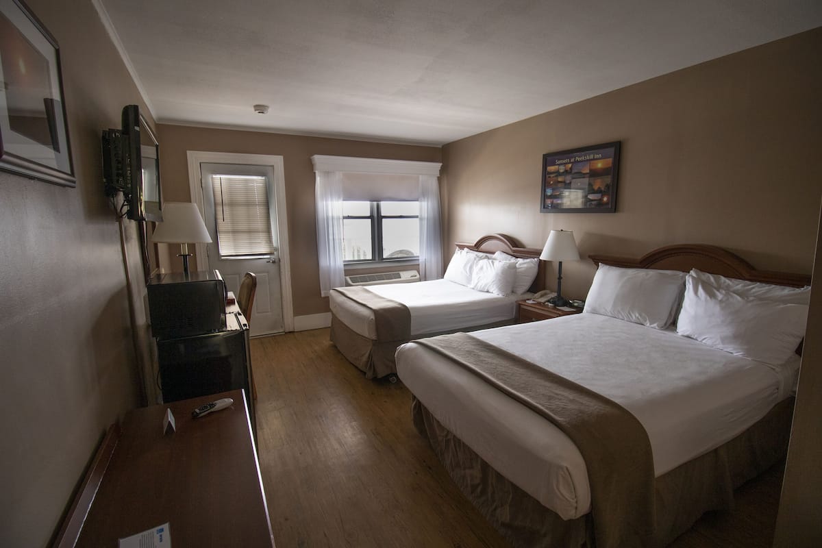 Habitación de hotel con dos camas, un escritorio, una silla, una ventana con persianas y una puerta.