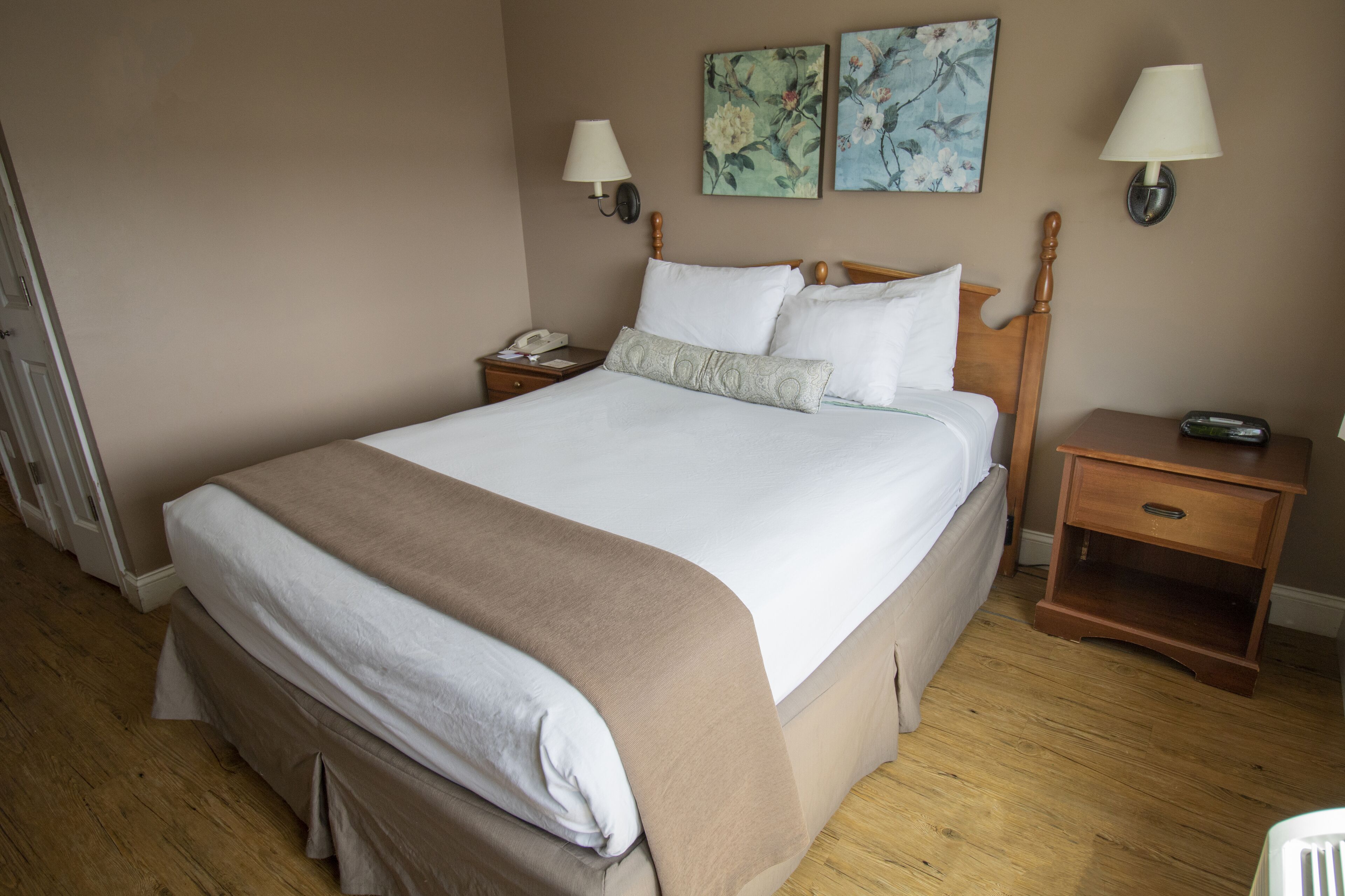 Una cama bien hecha con un cabecero de madera, dos mesitas de noche con lámparas y una obra de arte floral en la pared.