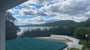 Une vue depuis une véranda couverte donnant sur un lac, avec une clôture blanche et des arbres au premier plan.