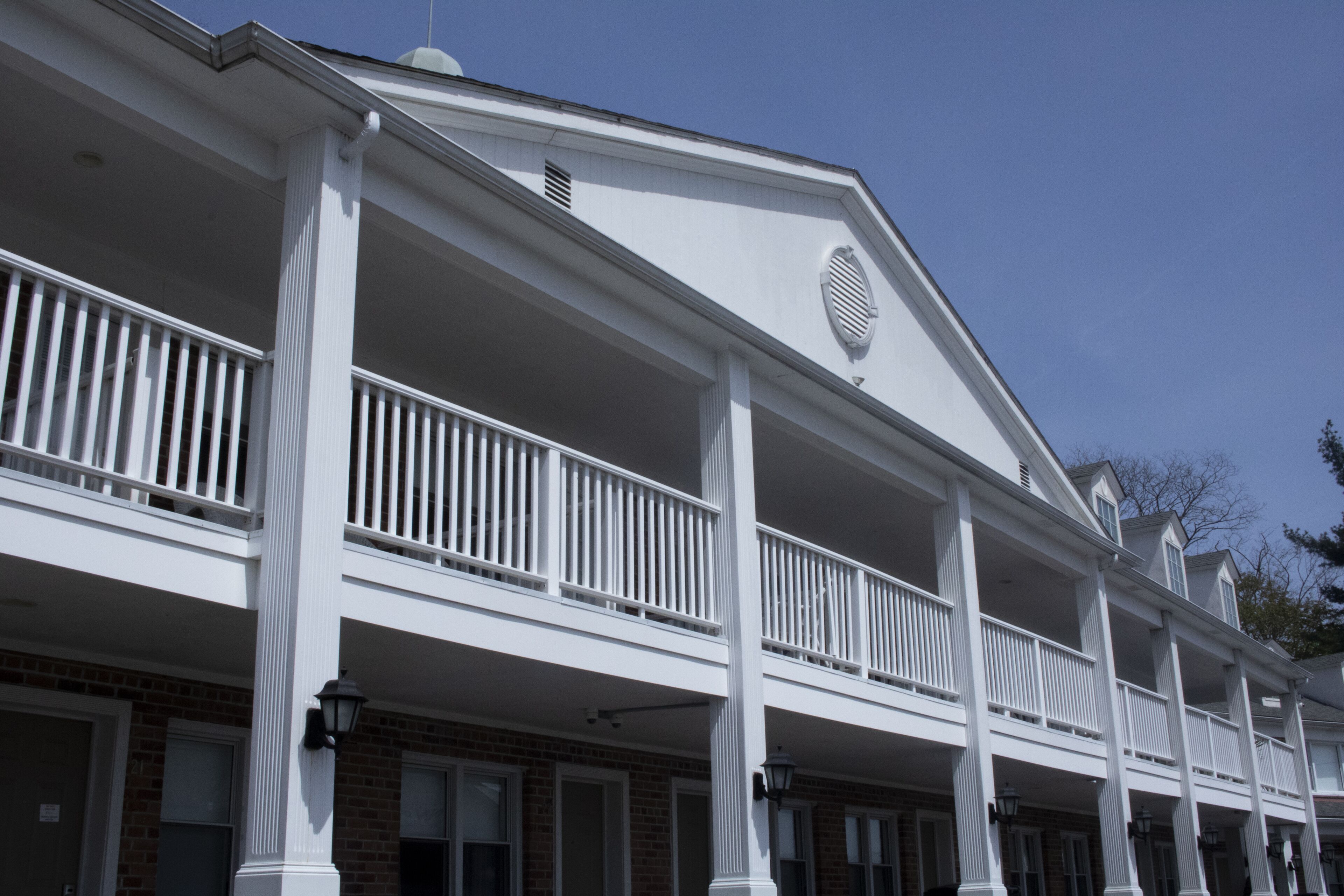 A two-story building with a white exterior, multiple balconies, and a brick facade.