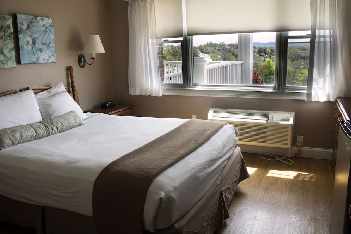 Habitación de hotel con una cama grande, ventana con vistas a la ciudad, lámpara de pared y termostato.