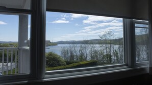 Une vue depuis une fenêtre donnant sur un lac, avec des arbres et des collines en arrière-plan.