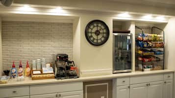 Una barra de desayuno con una máquina de café, un reloj y estantes llenos de aperitivos y bebidas.