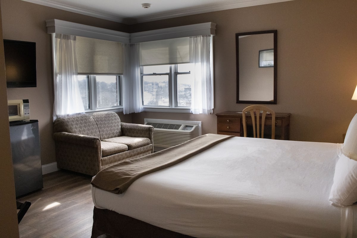 Habitación de hotel con una cama grande, un sofá, un escritorio y una ventana con cortinas.