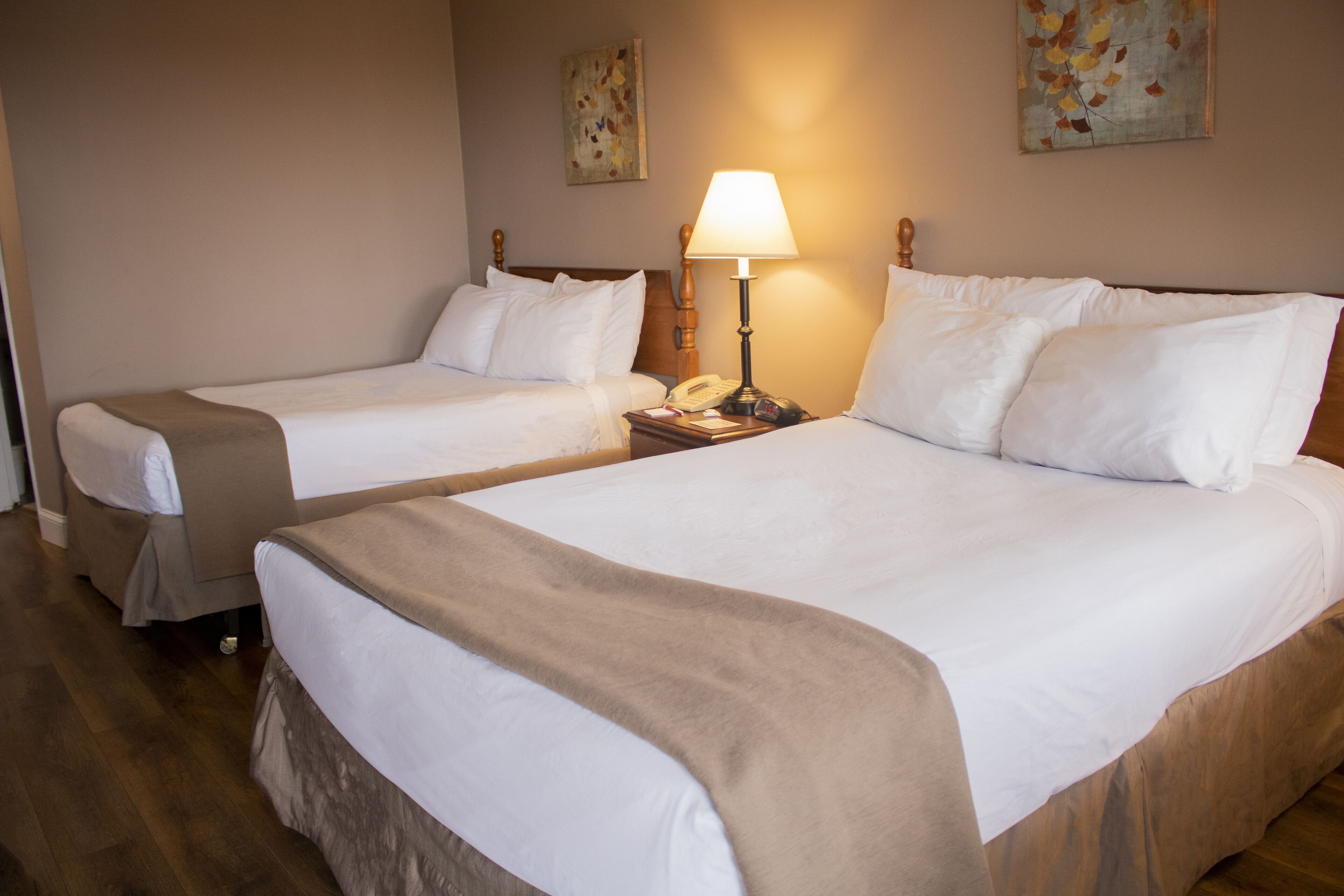A hotel room with two beds, a bedside lamp, and artwork on the walls.