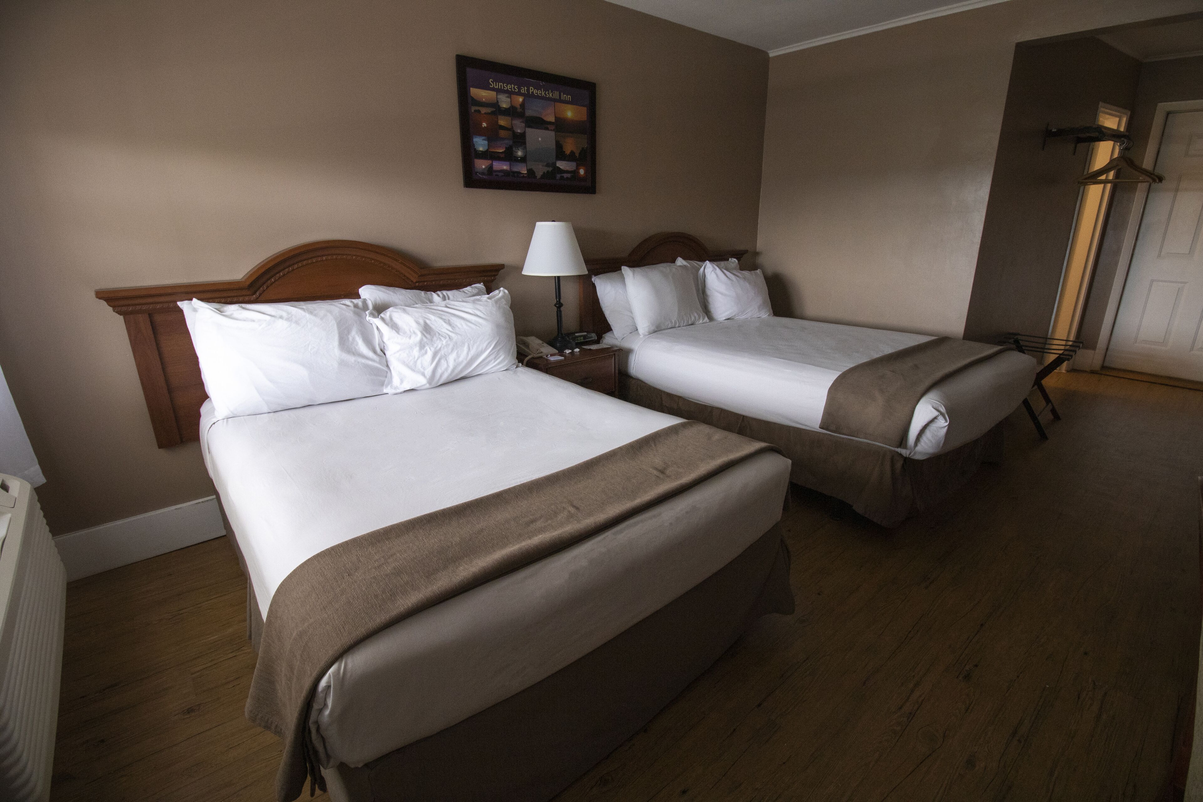 A hotel room with two beds, a nightstand, a lamp, and a framed picture on the wall.