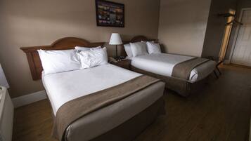 A hotel room with two beds, a nightstand, a lamp, and a framed picture on the wall.