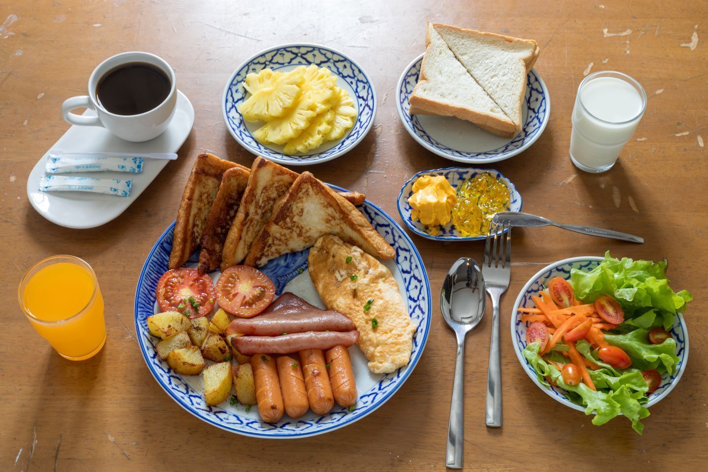 A breakfast table with toast, eggs, sausages, potatoes, tomatoes, and a salad.