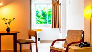 A room with a wooden chair, a small table with a vase, a window with curtains, and a lamp. - Collection O Howard Square Boutique Hotel (Bangkok)