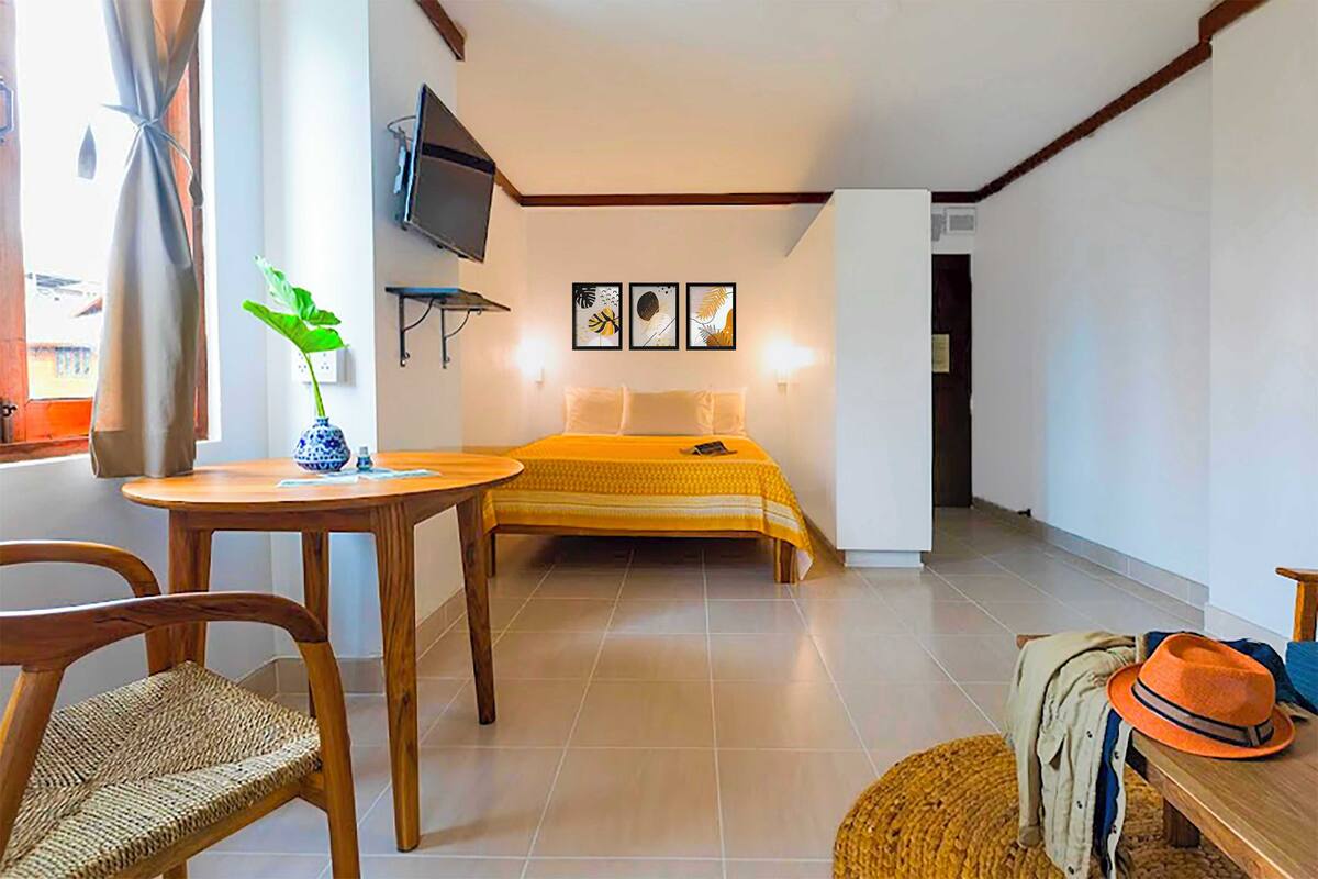 A hotel room with a bed, a TV mounted on the wall, a small table with a vase, and a chair.