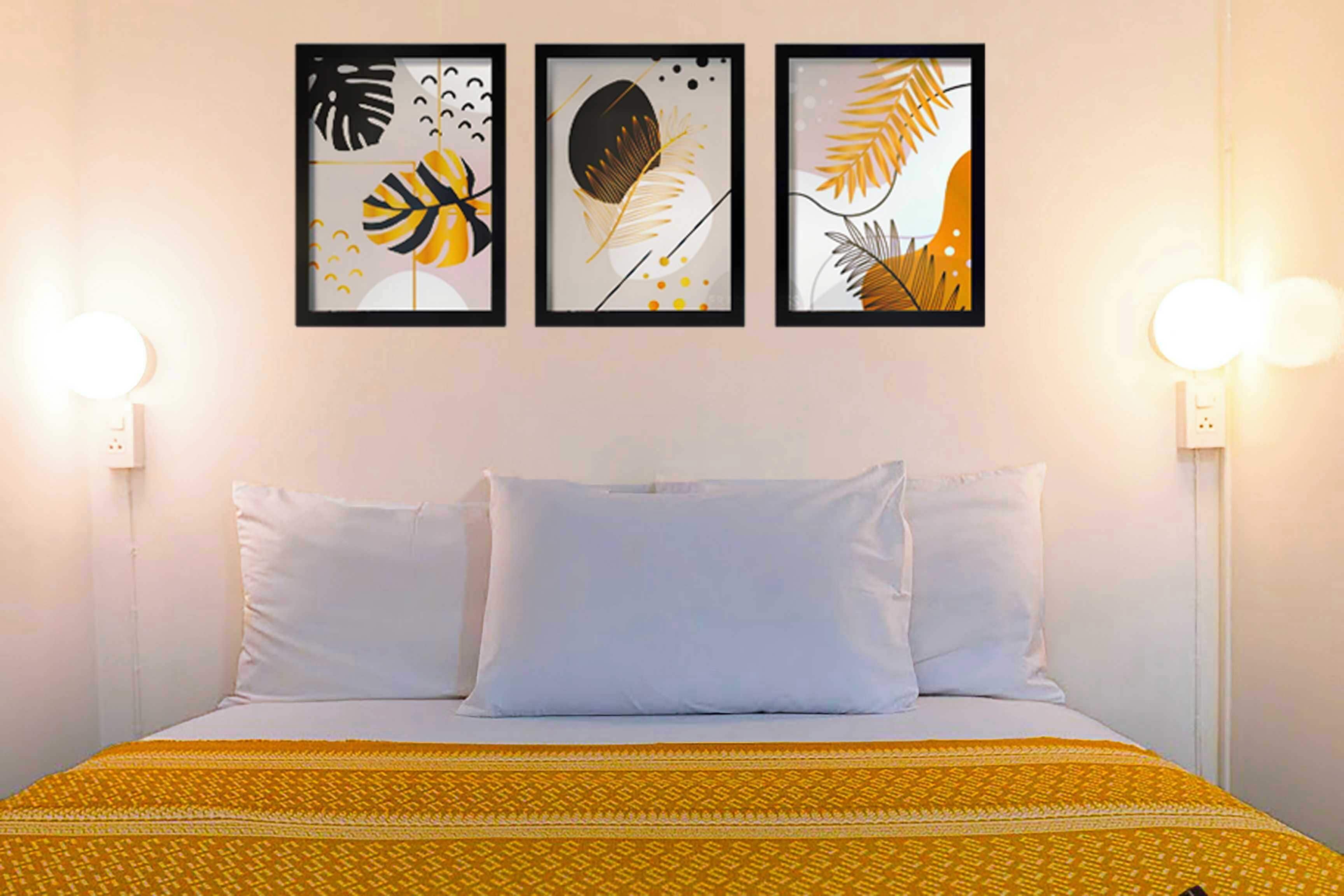 A bed with white bedding, a yellow patterned blanket, and three framed artworks above it.
