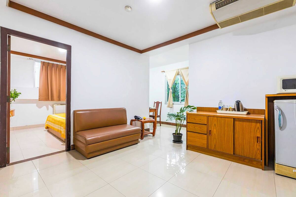 A room with a brown sofa, wooden cabinet, and a small kitchenette.