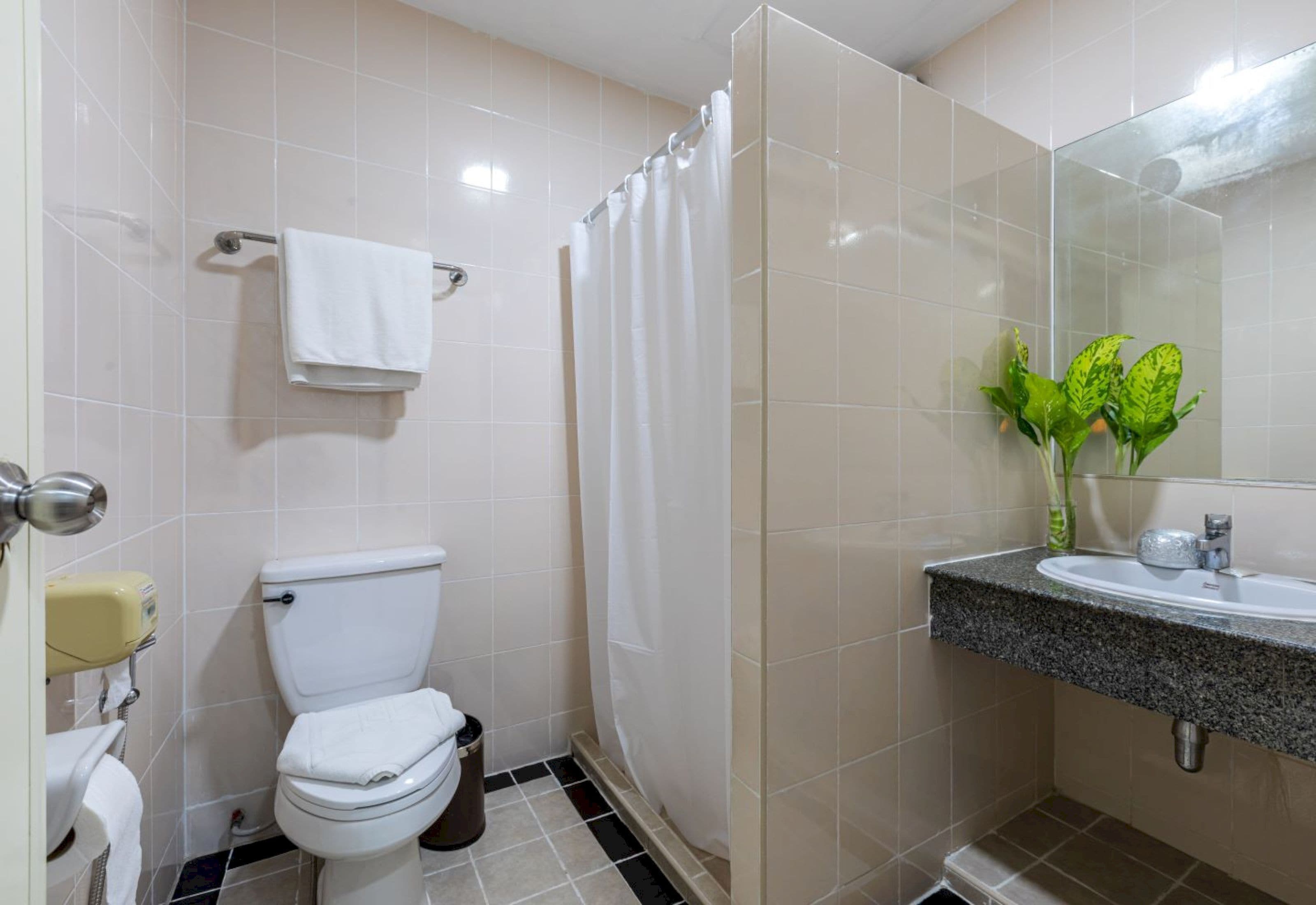 A bathroom with a toilet, a shower curtain, a sink with a mirror, and a plant.