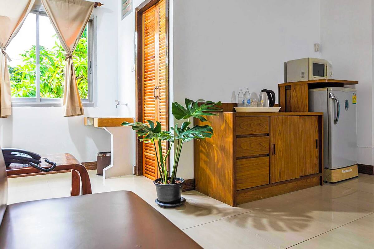 A room with a wooden cabinet, a refrigerator, a microwave, a potted plant, a telephone, and a window with curtains.