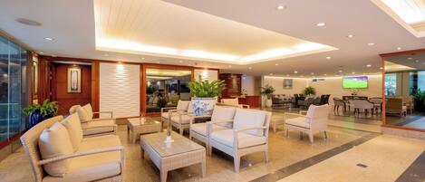 A spacious lobby with a modern design, featuring a seating area with sofas and chairs, a coffee table, and a large TV screen.