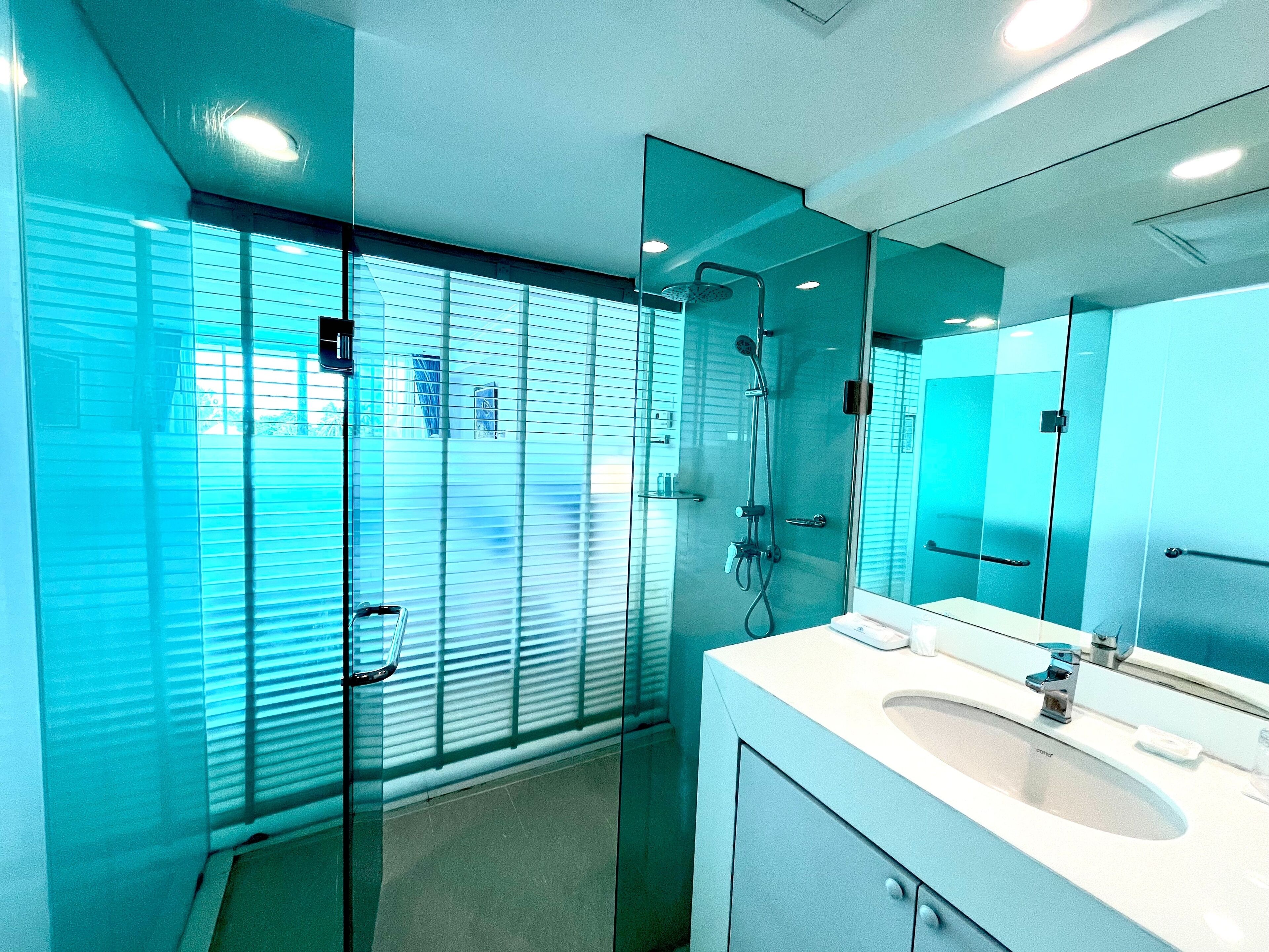 Un baño moderno con cabina de ducha de vidrio, lavamanos blanco y un espejo grande.