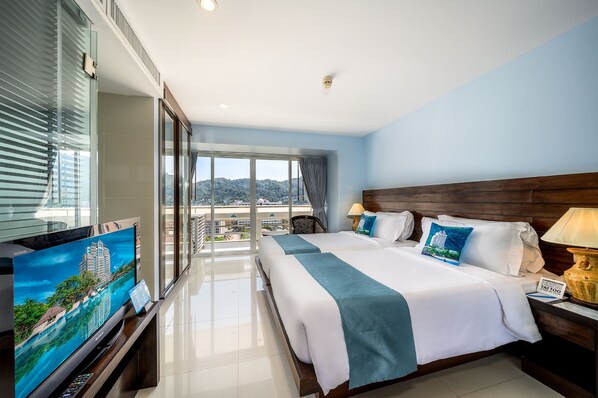 A hotel room with a large TV, two beds, a balcony with a city view, and a wooden headboard. - Andaman Beach Suites Hotel (Patong)