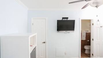 A bedroom with a TV mounted on the wall, a ceiling fan, and a door leading to a bathroom.