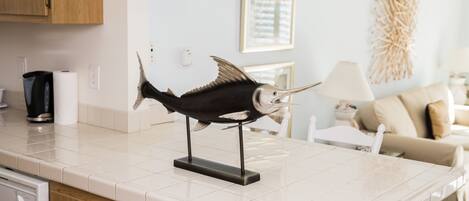 Et køkken med en fiskeskulptur på bordpladen, træskabe, en hvid bordplade og et spiseområde med et bord og stole.