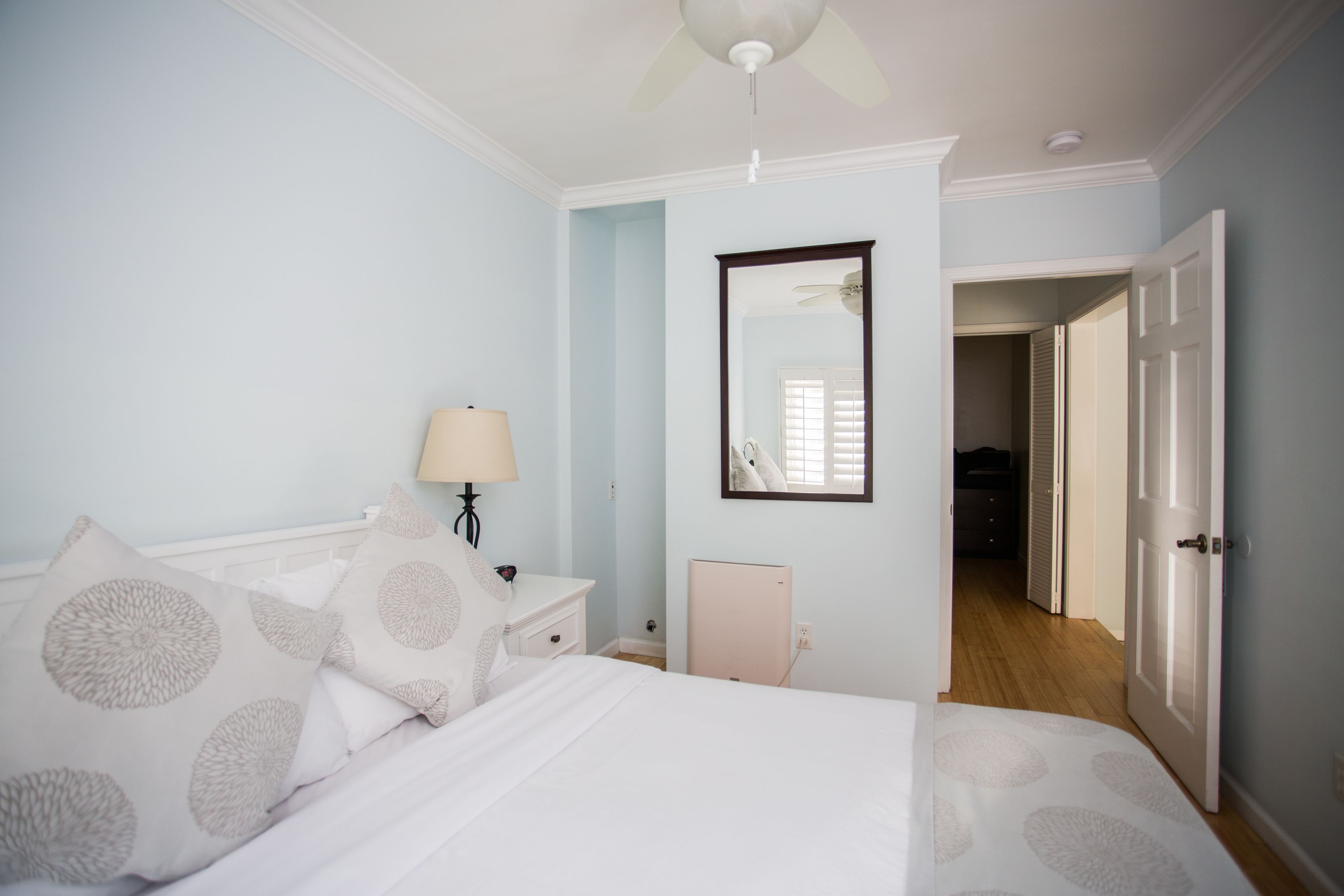 Un dormitorio con cama, mesita de noche, lámpara y una puerta que da a otra habitación.
