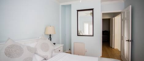 Un dormitorio con cama, mesita de noche, lámpara y una puerta que da a otra habitación.