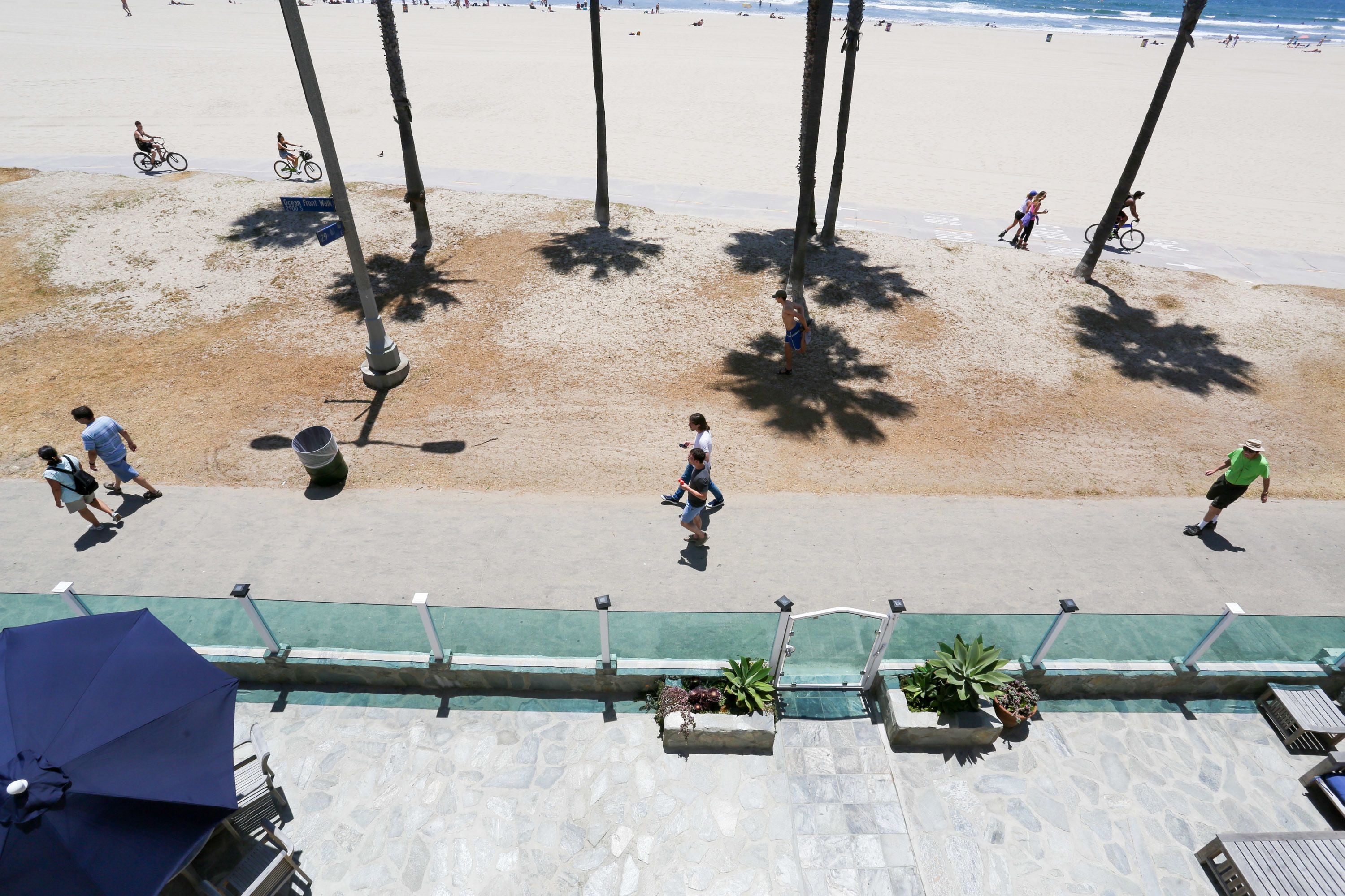 Una platja amb palmeres, cel serè i persones caminant i pedalant.