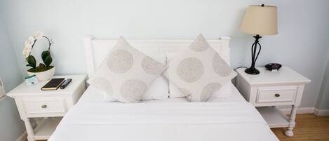 Una cama bien hecha con dos almohadas decorativas, una mesita de noche con una lámpara, un control remoto y una planta en maceta.
