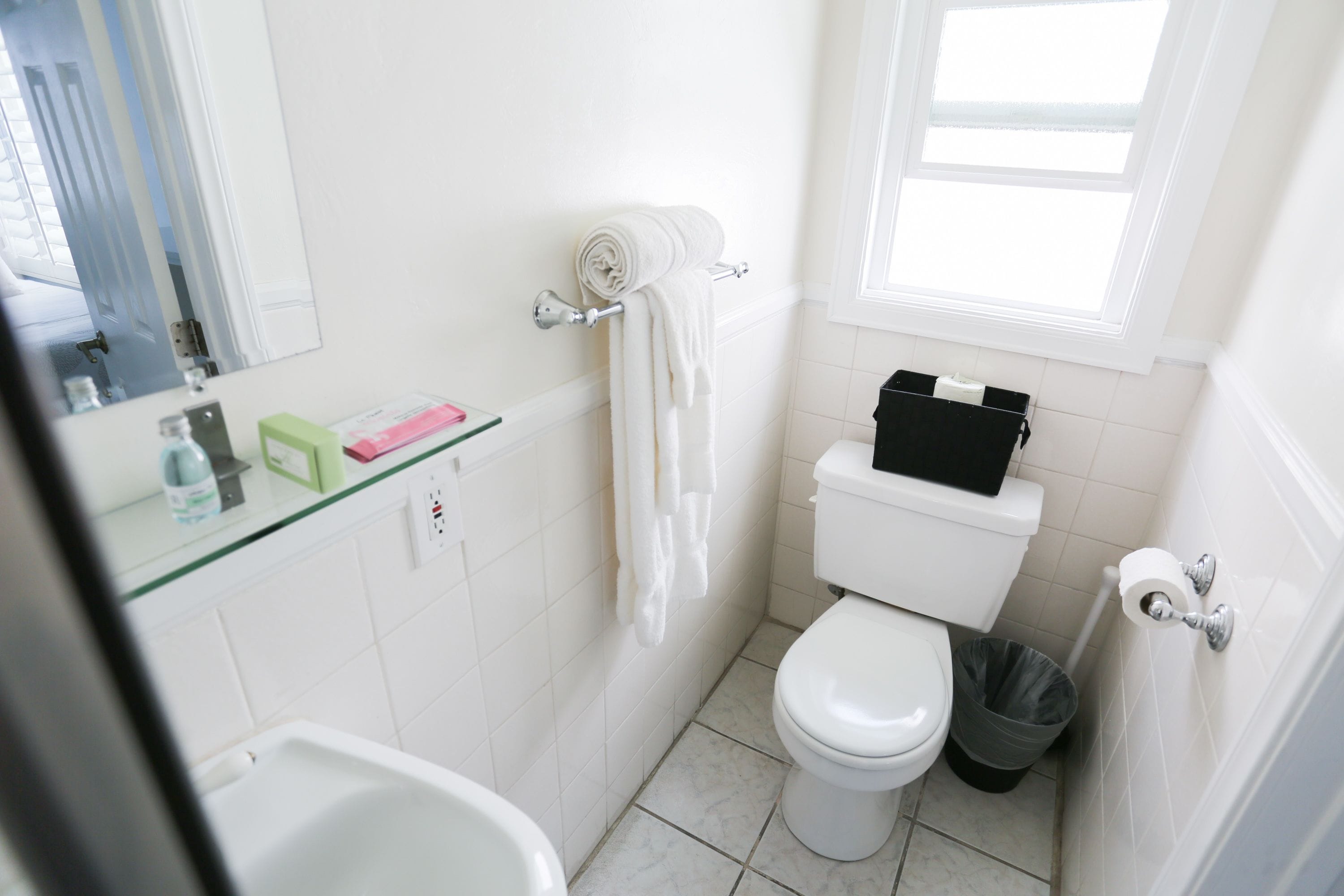 Ein Badezimmer mit Toilette, Waschbecken, Duschkabine aus Glas, Handtuchhalter und einem Fenster.