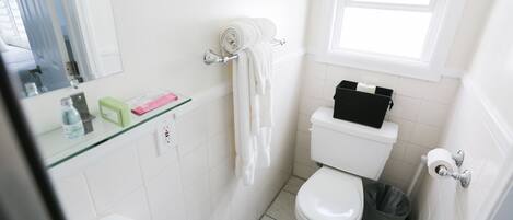 Ein Badezimmer mit Toilette, Waschbecken, Duschkabine aus Glas, Handtuchhalter und einem Fenster.