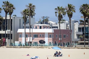 A beachfront hotel with a prominent pink building, palm trees, and beach umbrellas.