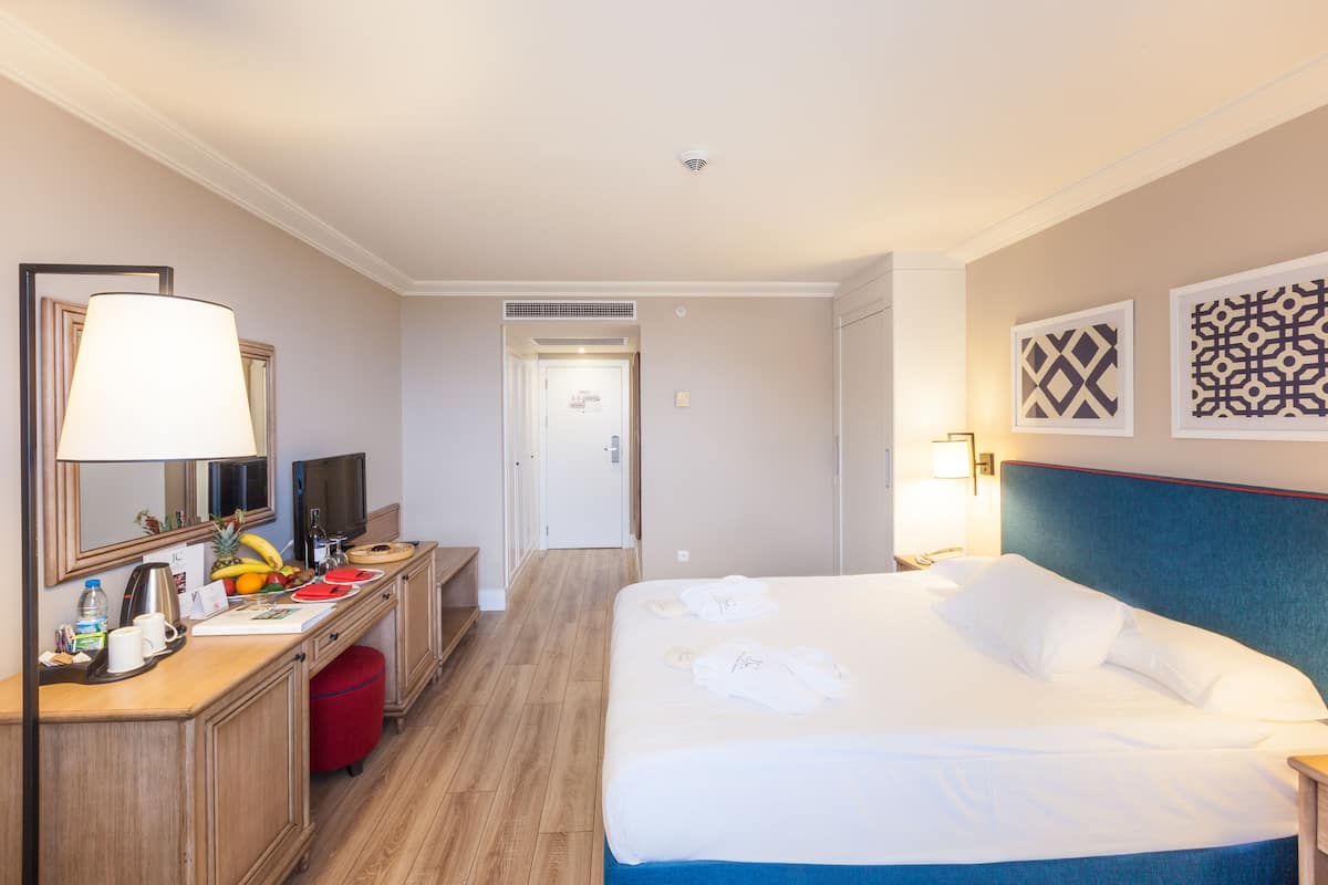 Una habitación de hotel con cama, escritorio con lámpara, televisión y puerta que da a otra habitación.