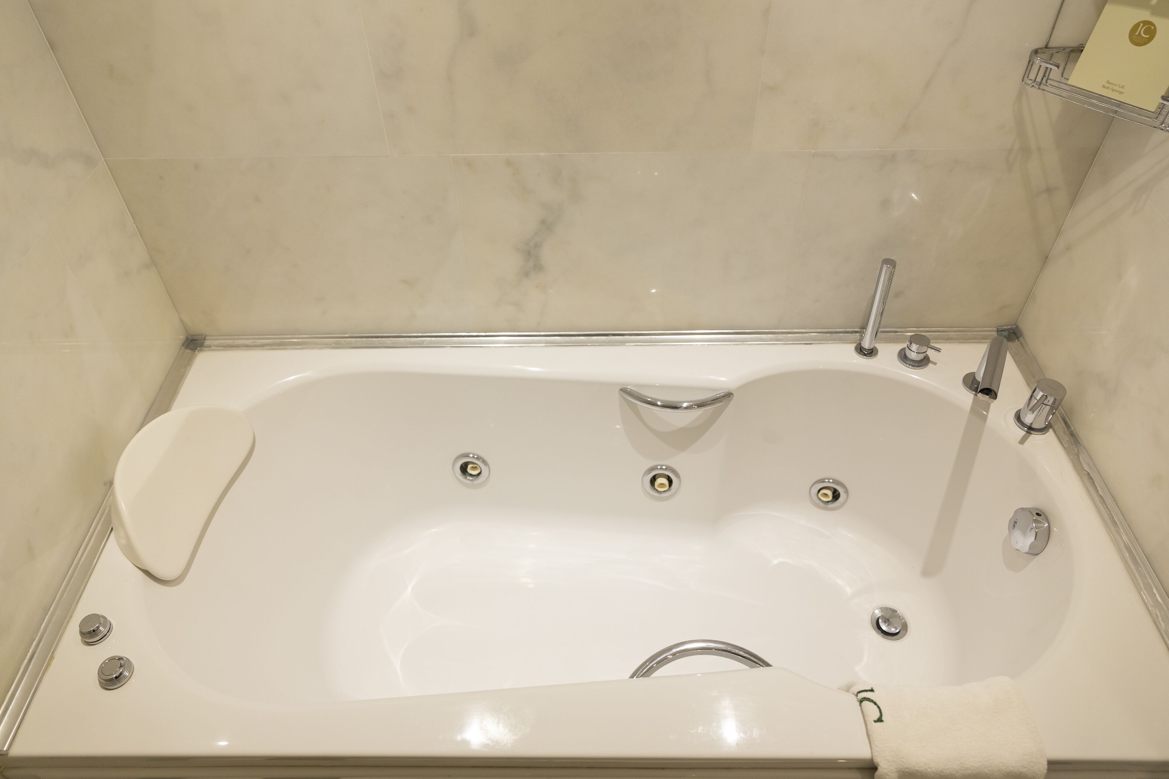 Una bañera blanca con cabezal de ducha manual, asiento integrado y un perchero.