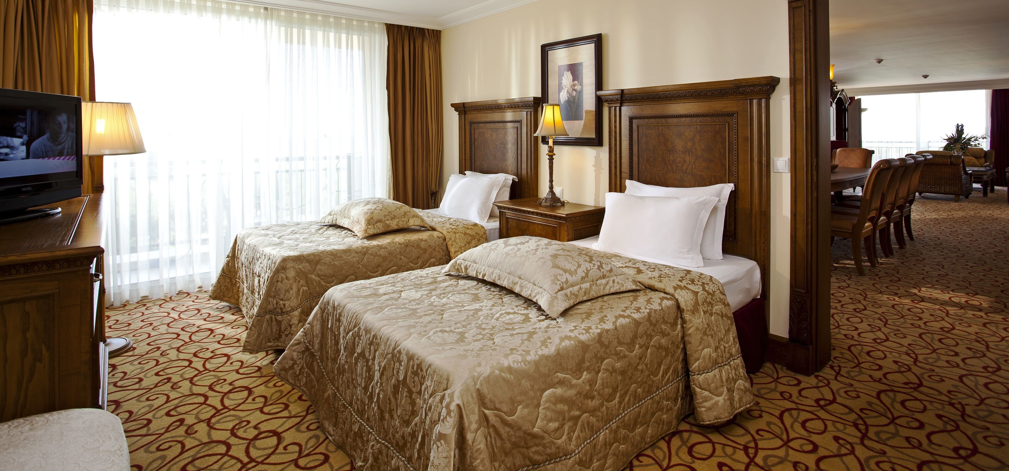 A hotel room with two beds, a television, and a dining area with chairs.