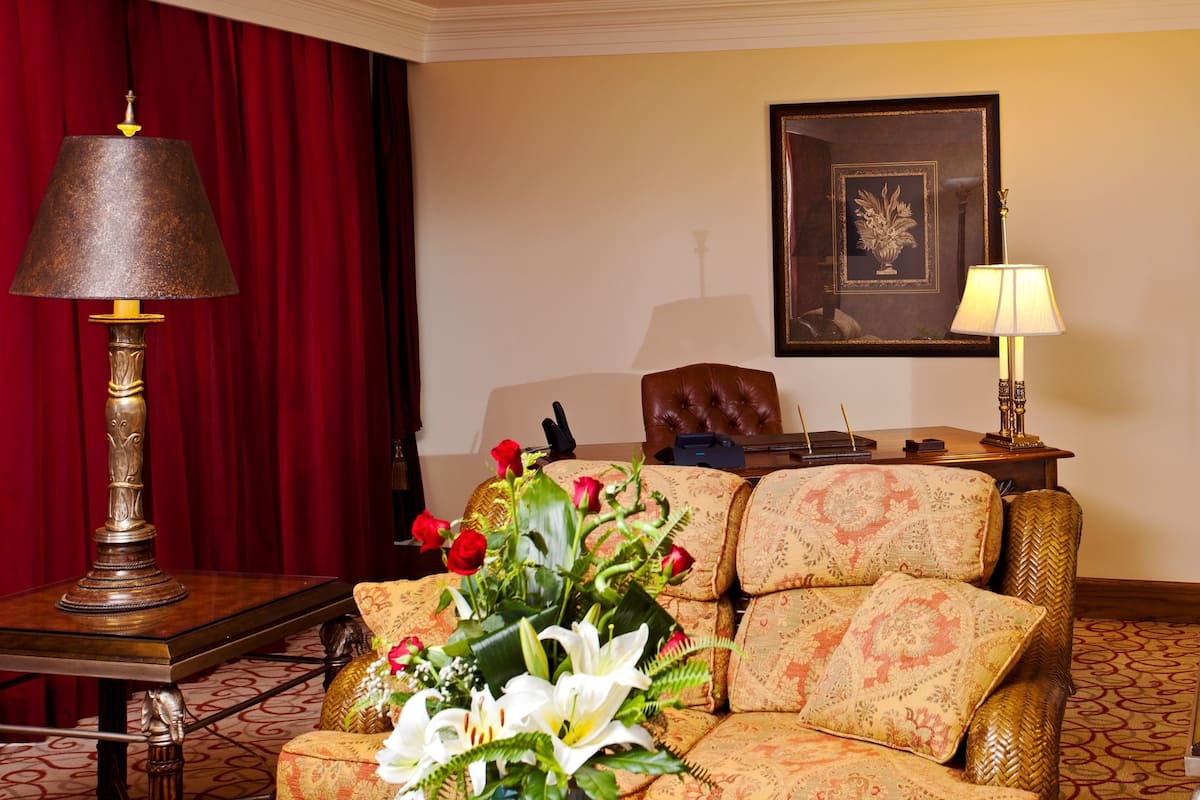 Una habitación con un sofá, dos lámparas, un cuadro enmarcado y una cortina roja.