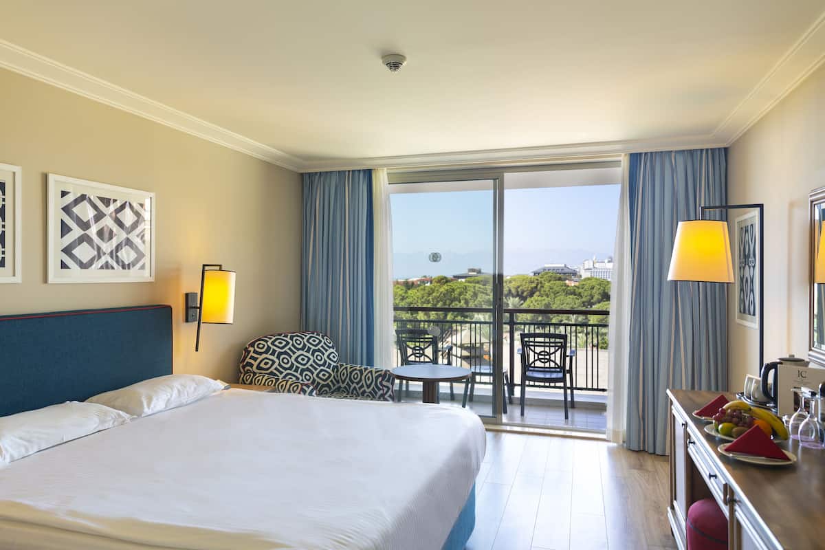 Habitación de hotel con una cama grande, un balcón con mesa y sillas, y vistas a la ciudad.