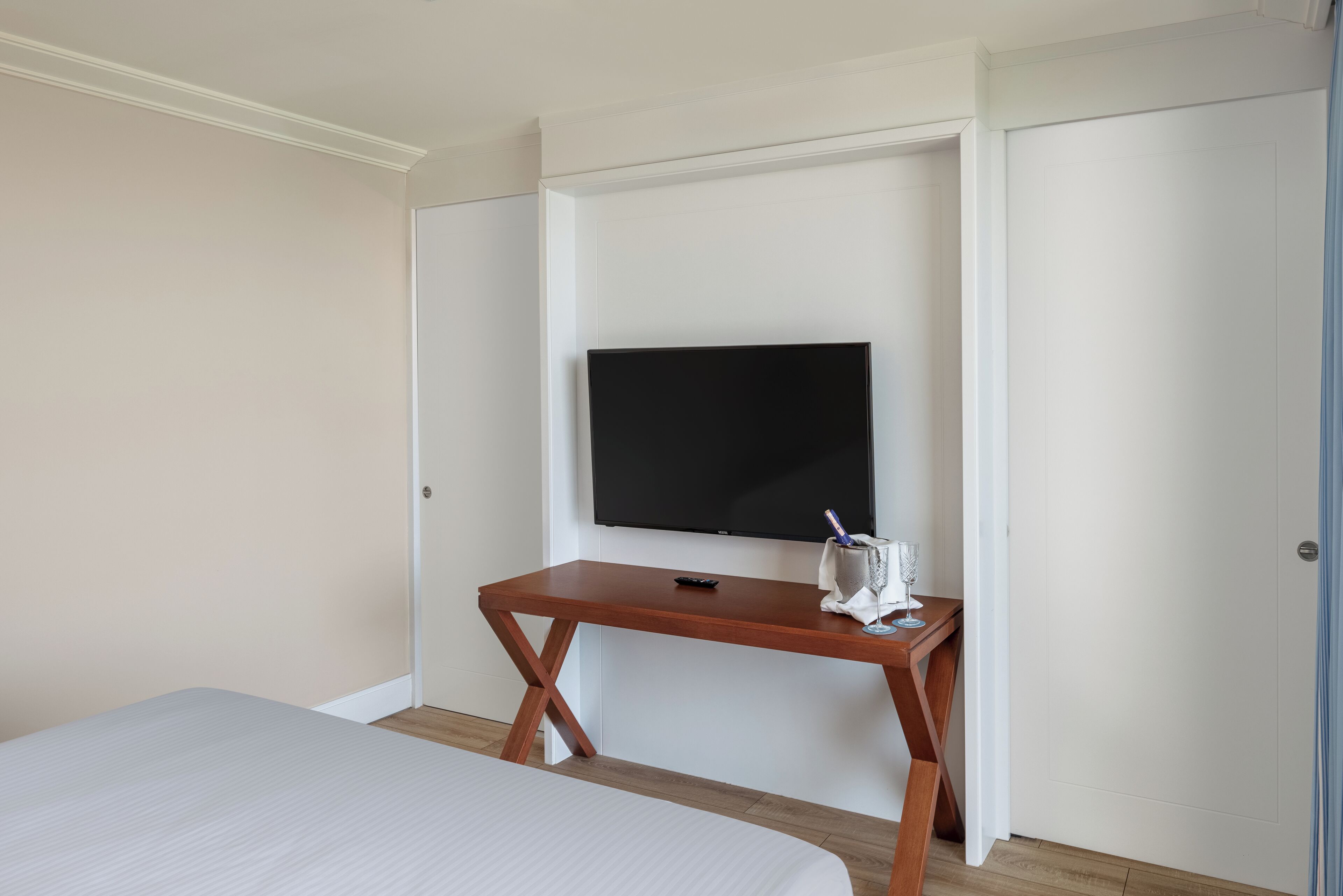 Una habitación de hotel con una cama, un escritorio de madera, un televisor de pantalla plana y una puerta.