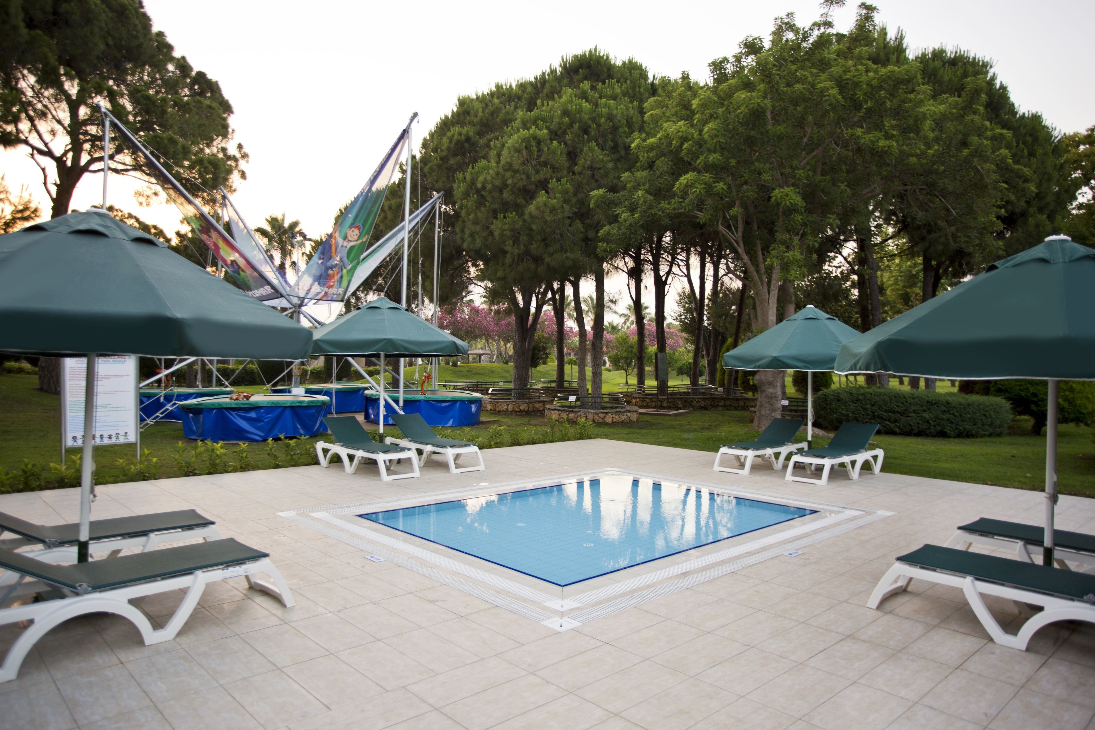 A swimming pool with lounge chairs and umbrellas, surrounded by trees and a covered area.