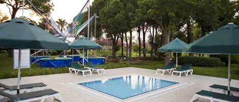 A swimming pool with lounge chairs and umbrellas, surrounded by trees and a covered area.