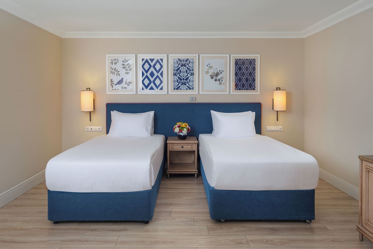 Habitación doble con dos camas, una mesita de noche con un florero y decoración en la pared.