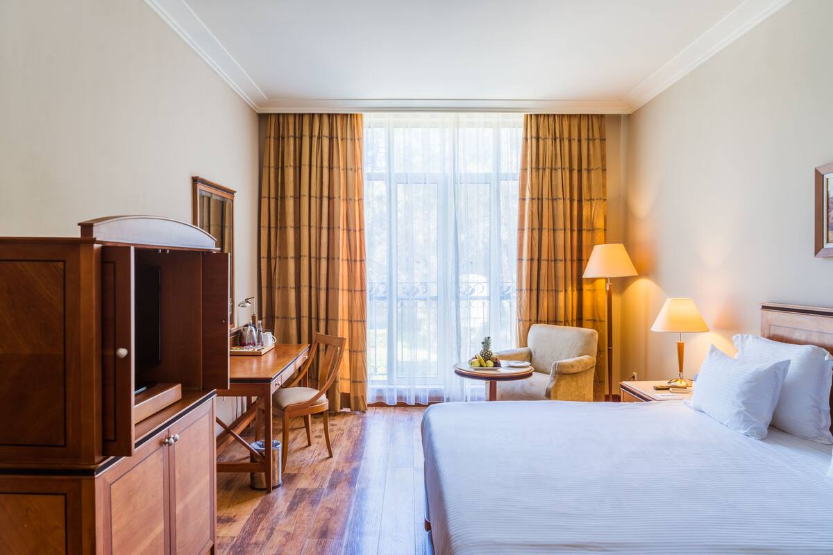 A hotel room with a bed, a desk, a chair, a lamp, and a television.