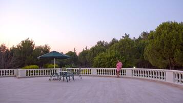 An outdoor patio with a table and chairs, a green umbrella, and a white balustrade.