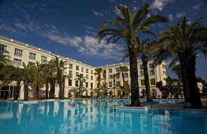 A large hotel with a swimming pool surrounded by palm trees.