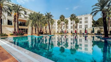 Una amplia piscina al aire libre rodeada de palmeras y un edificio imponente con múltiples balcones.